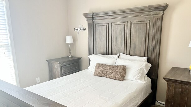 A bedroom with a large bed, a nightstand with a lamp, and a wall-mounted sign.