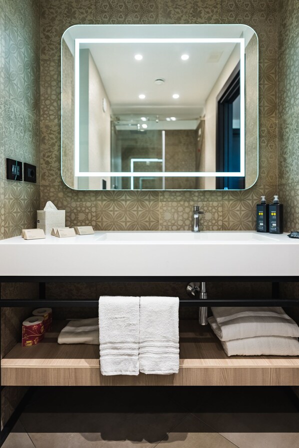 Un baño moderno con un espejo grande, un lavabo blanco y dos toalleros.