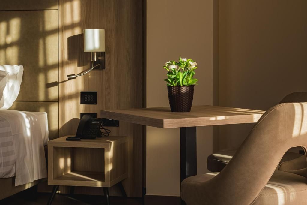Habitación de hotel con cama, mesita de noche, lámpara, teléfono y una planta en maceta.