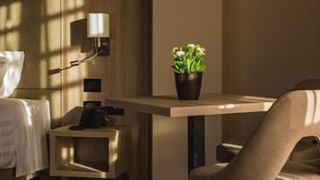 Habitación de hotel con cama, mesita de noche, lámpara, teléfono y una planta en maceta.