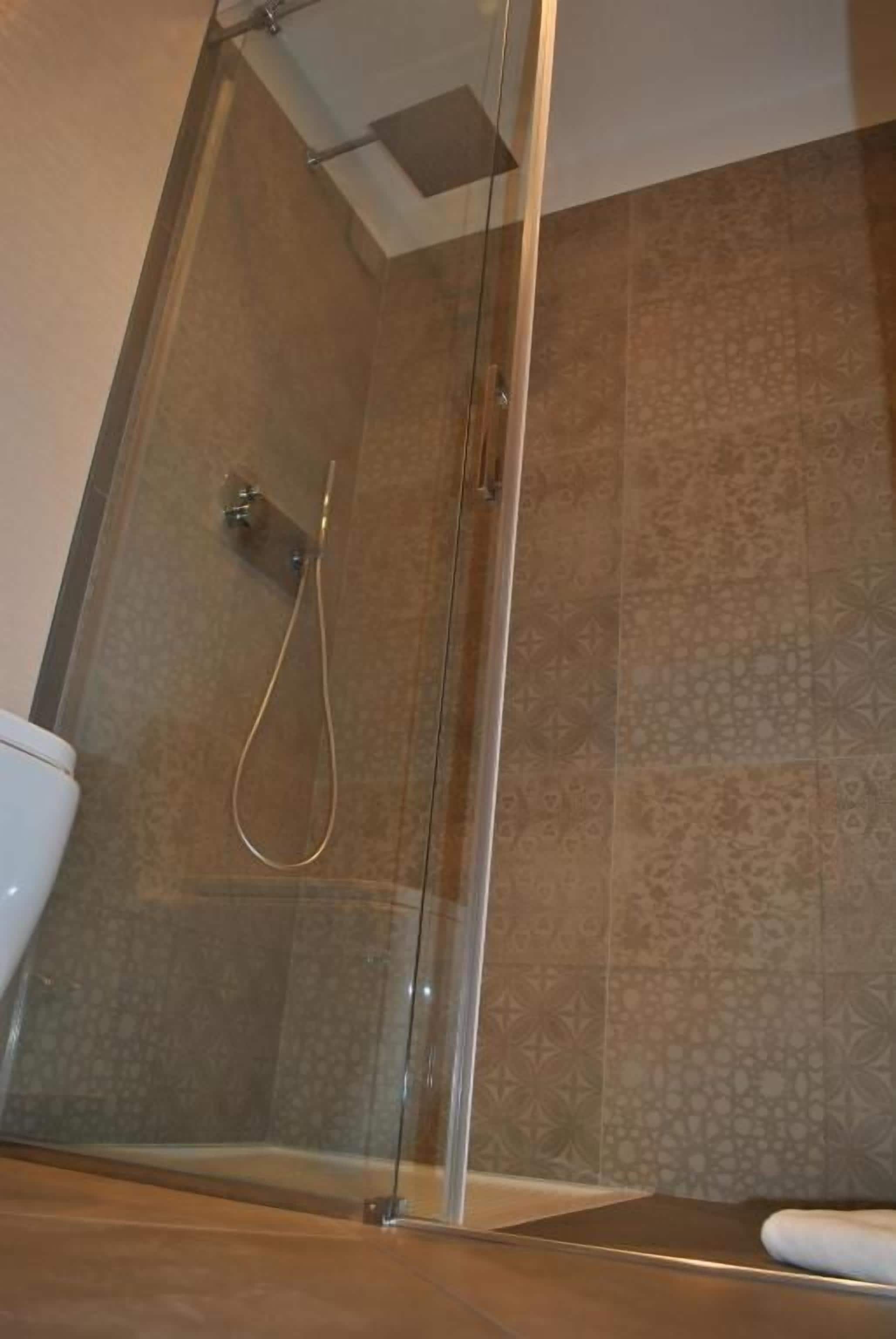 A glass-enclosed shower area with a showerhead and a control panel.
