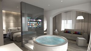 Una habitación de hotel moderna con un televisor grande montado en la pared que muestra diversas aplicaciones, una zona de estar acogedora con sofá y sillón, una mesita y una bañera de hidromasaje circular.
