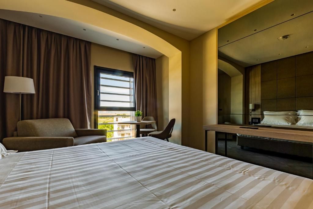 A hotel room with a large bed, a desk, a chair, and a window with curtains.