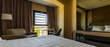 A hotel room with a large bed, a desk, a chair, and a window with curtains.