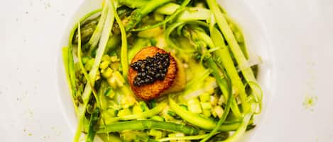 Une assiette de nourriture garnie d’une noix de Saint-Jacques et de caviar, le tout entouré de légumes verts.