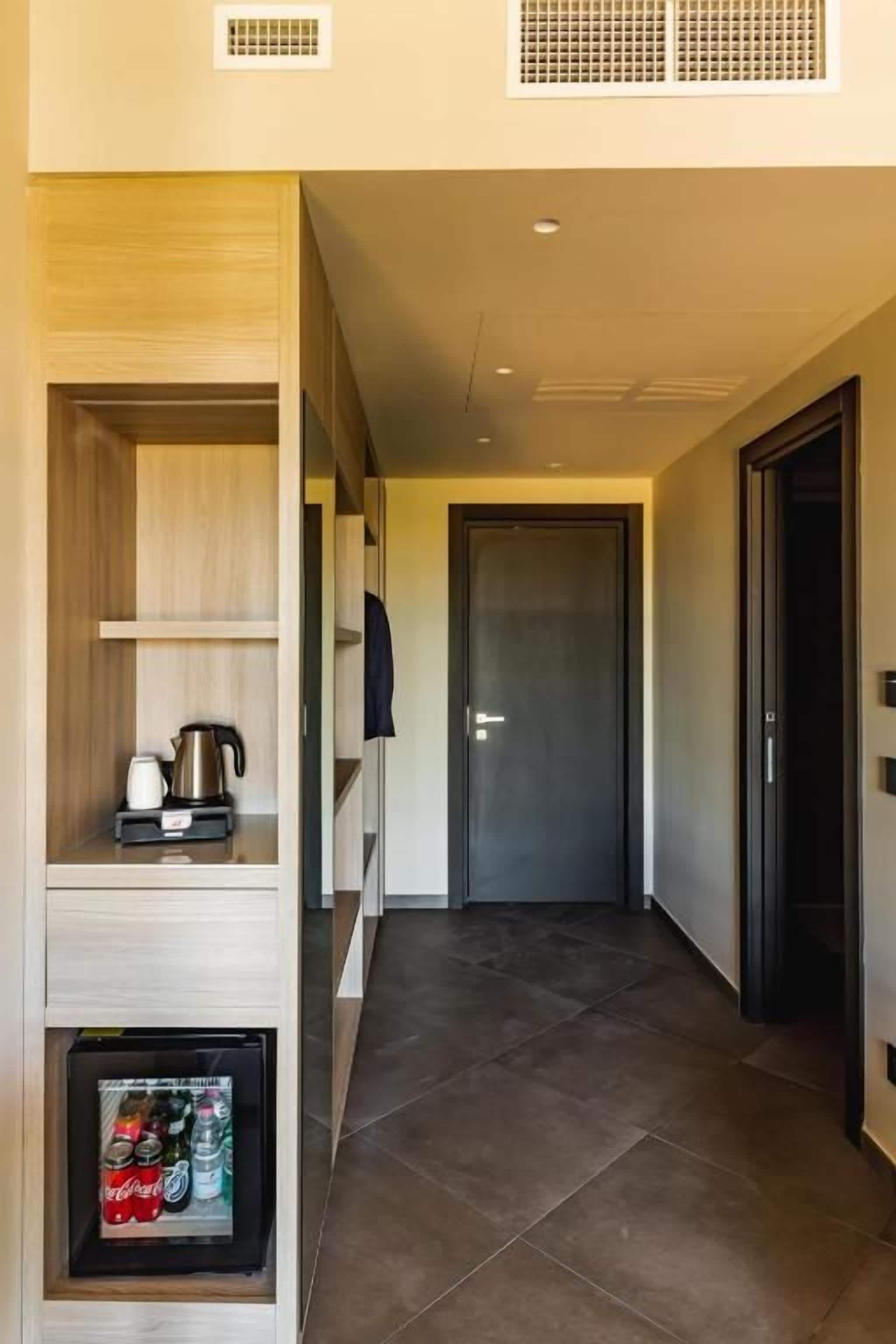 Um corredor com estante de madeira embutida, um frigorífico com bebidas e uma porta no final.