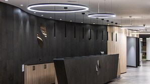 Una moderna recepción con encimera de madera oscura y una elegante barra negra, con luces circulares en el techo.