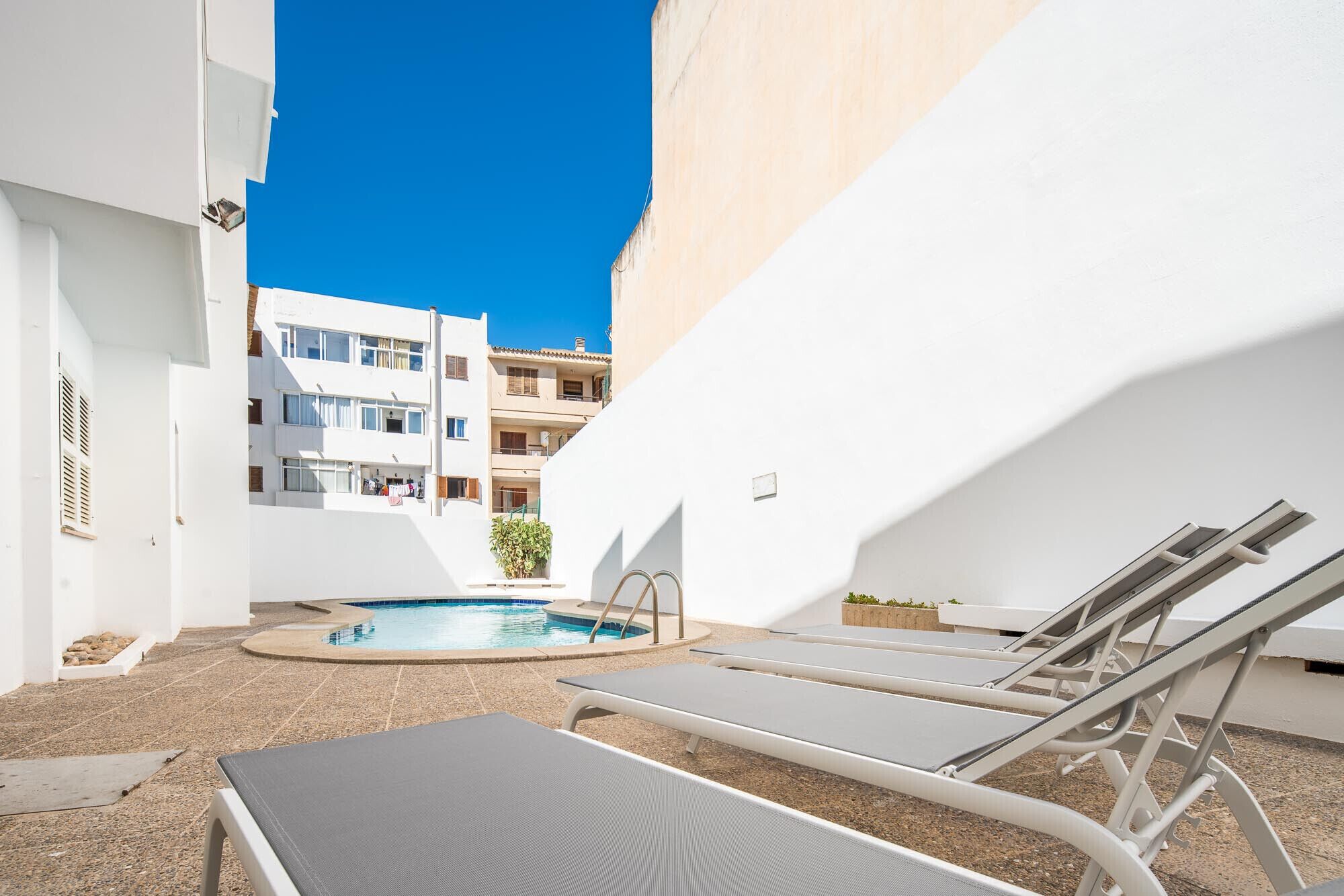 A pool area with lounge chairs, a small pool, and a building in the background.