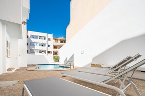 Un espace piscine avec des chaises longues, une petite piscine et un bâtiment en arrière-plan.