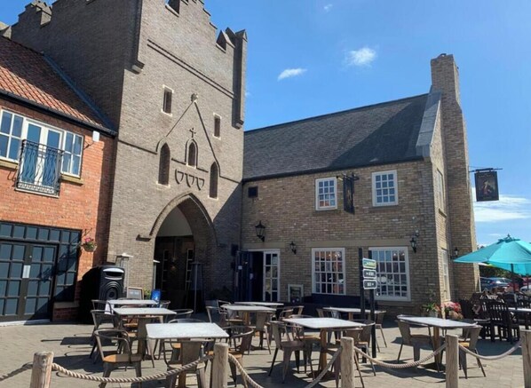 A building with a tower, outdoor seating area, and a sign indicating a restaurant. - Sandy Feet 1st floor apartment with open plan living on The Bay, Filey (Primrose Valley)
