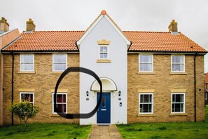 A two-story house with a blue front door, a brick facade, and a tiled roof. - Sandy Feet 1st floor apartment with open plan living on The Bay, Filey (Primrose Valley)