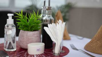 A table with a red placemat, a small potted plant, a glass bottle with a pump, a container labeled "Salt", and a napkin holder with white napkins.