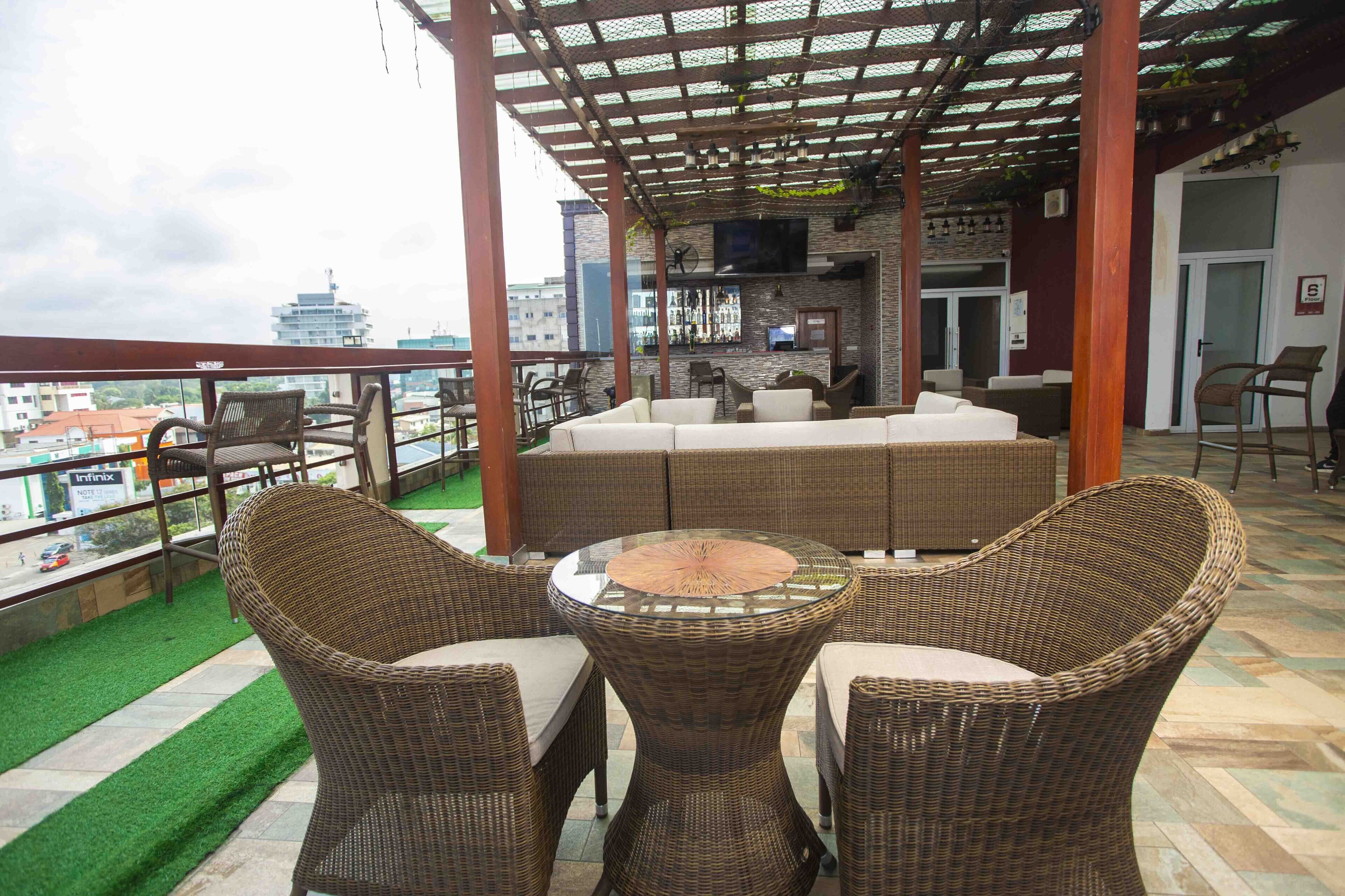 A covered outdoor seating area with wicker furniture, a bar, and a view of the cityscape.