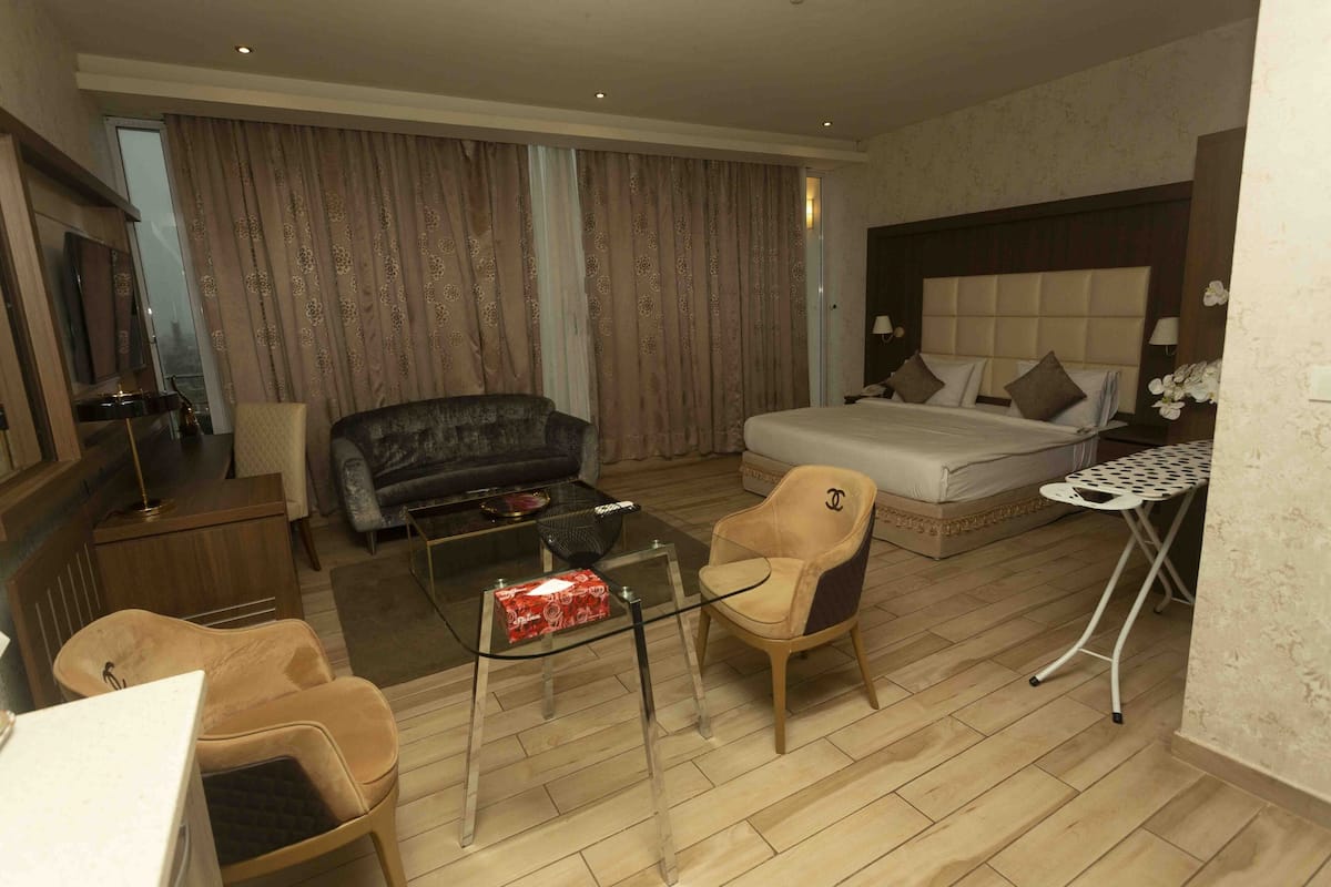 A hotel room with a bed, a sofa, a chair, a small table, and a TV.