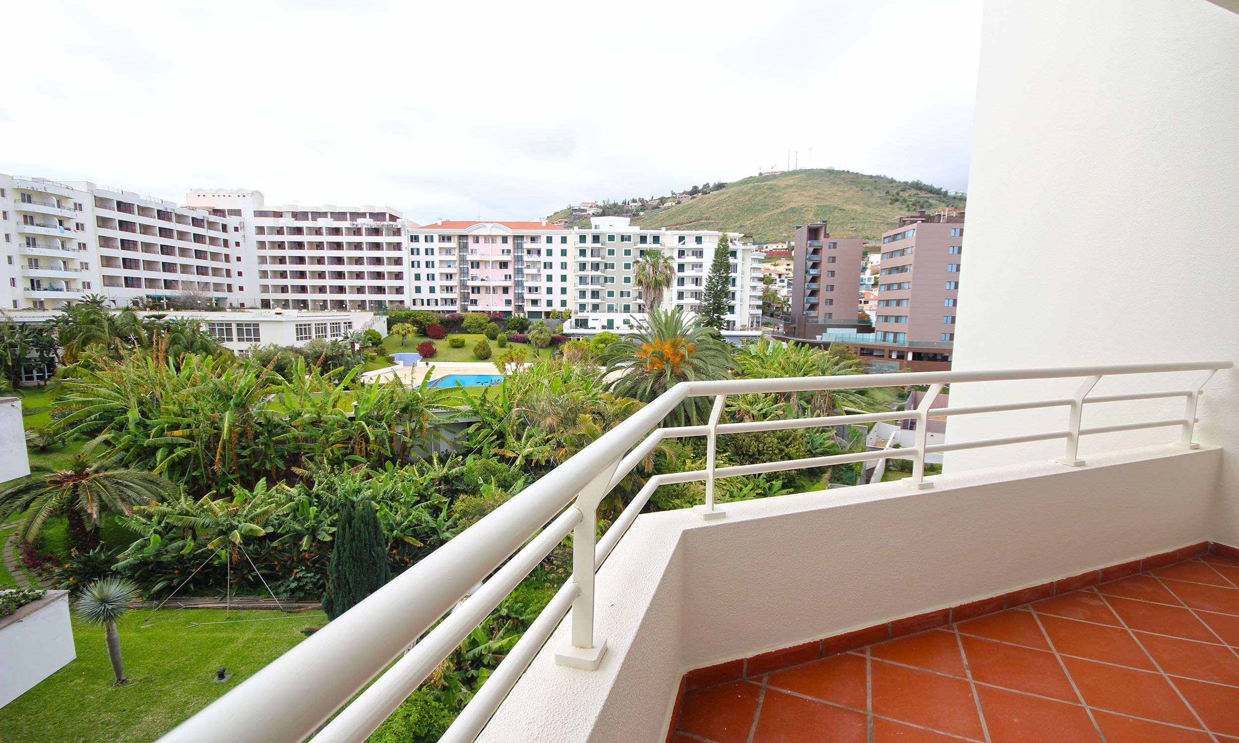 Un balcon offrant une vue sur un complexe hôtelier, une piscine et la végétation environnante.