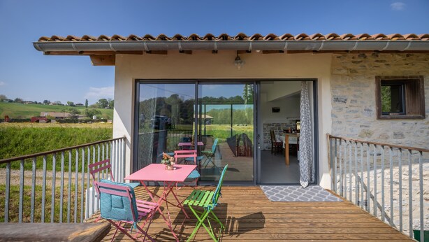 A wooden deck with outdoor seating, a glass door leading to an interior space, and a view of a green landscape.