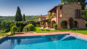 A pool with clear blue water, a stone building with arches, and a lush green garden. - Private villa with pool with panoramic view inside organic wine resort (Arezzo)