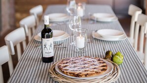 A dining table set with plates, glasses, a bottle of wine, and a dessert. - Private villa with pool with panoramic view inside organic wine resort (Arezzo)