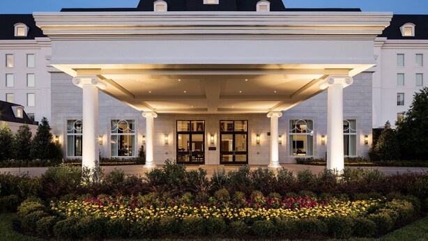 A grand hotel entrance with a covered patio, large columns, and a well-maintained garden with colorful flowers. - The Equestrian Hotel (Ocala)