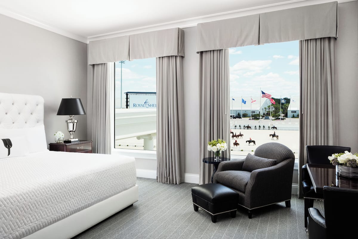 A hotel room with a large bed, a chair, a small table with flowers, and a view of a bridge and flags.