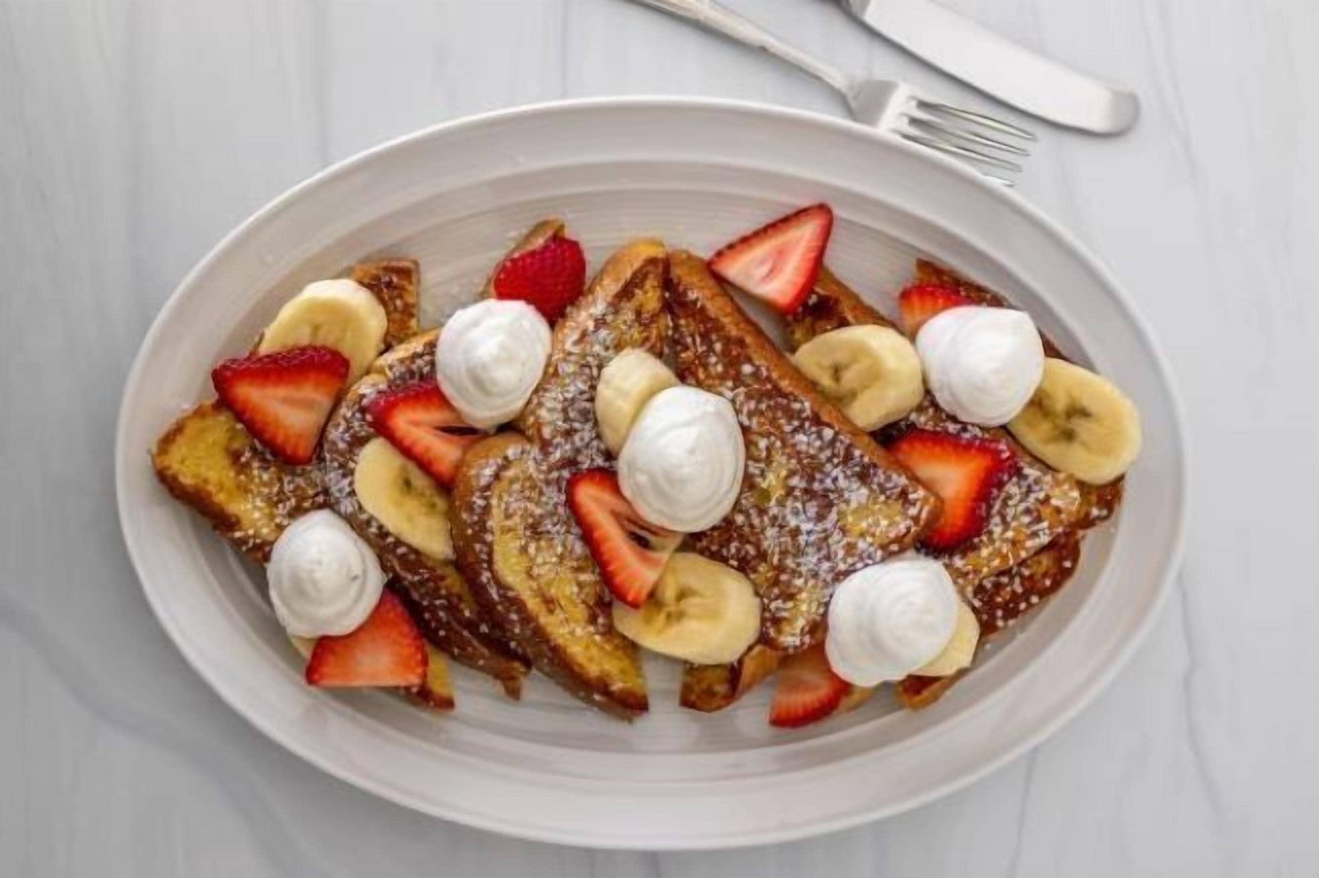 Un plato de tostadas francesas con fresas, plátanos y crema batida.
