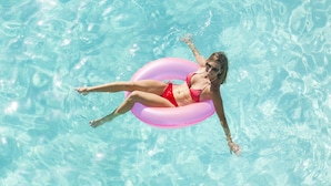 A person floating in a pool using a pink inflatable ring. - The Equestrian Hotel (Ocala)
