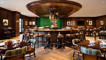 Zona de bar con barra central, diversas disposiciones de asientos y pared revestida de azulejos verdes.