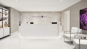 A reception area with a marble wall, a reception desk, white chairs, and a shelf with toiletries. - The Equestrian Hotel (Ocala)