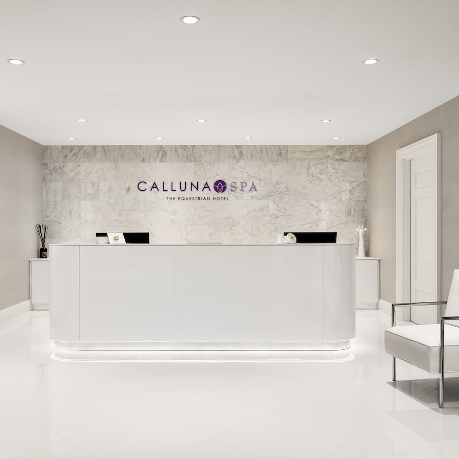 A reception area with a marble wall, a reception desk, white chairs, and a shelf with toiletries.