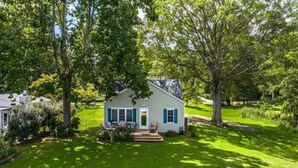 A single-story house with a front porch, surrounded by a well-maintained lawn and large trees. - Salty Air, Sandy Toes - Quiet Escape w/ Kayaks & Sandy Beach - 2BD waterfront (Heathsville)