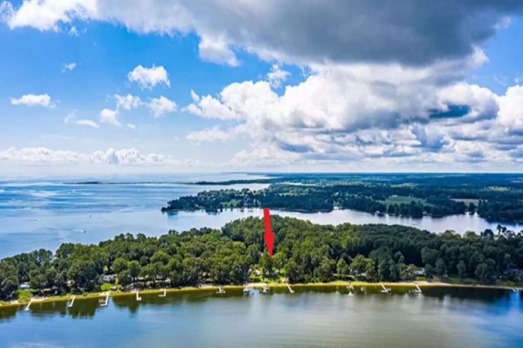 Vue aérienne d’une propriété au bord d’un lac, entourée d’une forêt dense, sous un ciel dégagé, avec un lac aux eaux calmes.