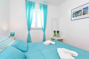 A bedroom with a bed, a nightstand, a window with curtains, a bedside table with a lamp, and a framed picture on the wall. - Holiday apartment with balcony, air conditioning and internet (Baška)