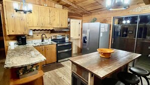 Una cucina in stile baita con mobili in legno, piani di lavoro in granito, un'isola centrale con sgabelli ed elettrodomestici integrati.