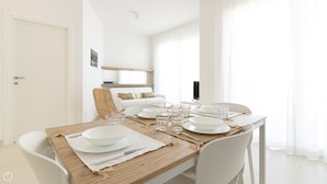 A dining area with a wooden table set for four, white chairs, and a white sofa in the background. - Rivazzurra Homes - 29 (Termoli)