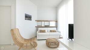 A modern living room with a white sofa, a wicker chair, a round wicker ottoman, a flat-screen TV, and a framed picture on the wall. - Rivazzurra Homes - 29 (Termoli)