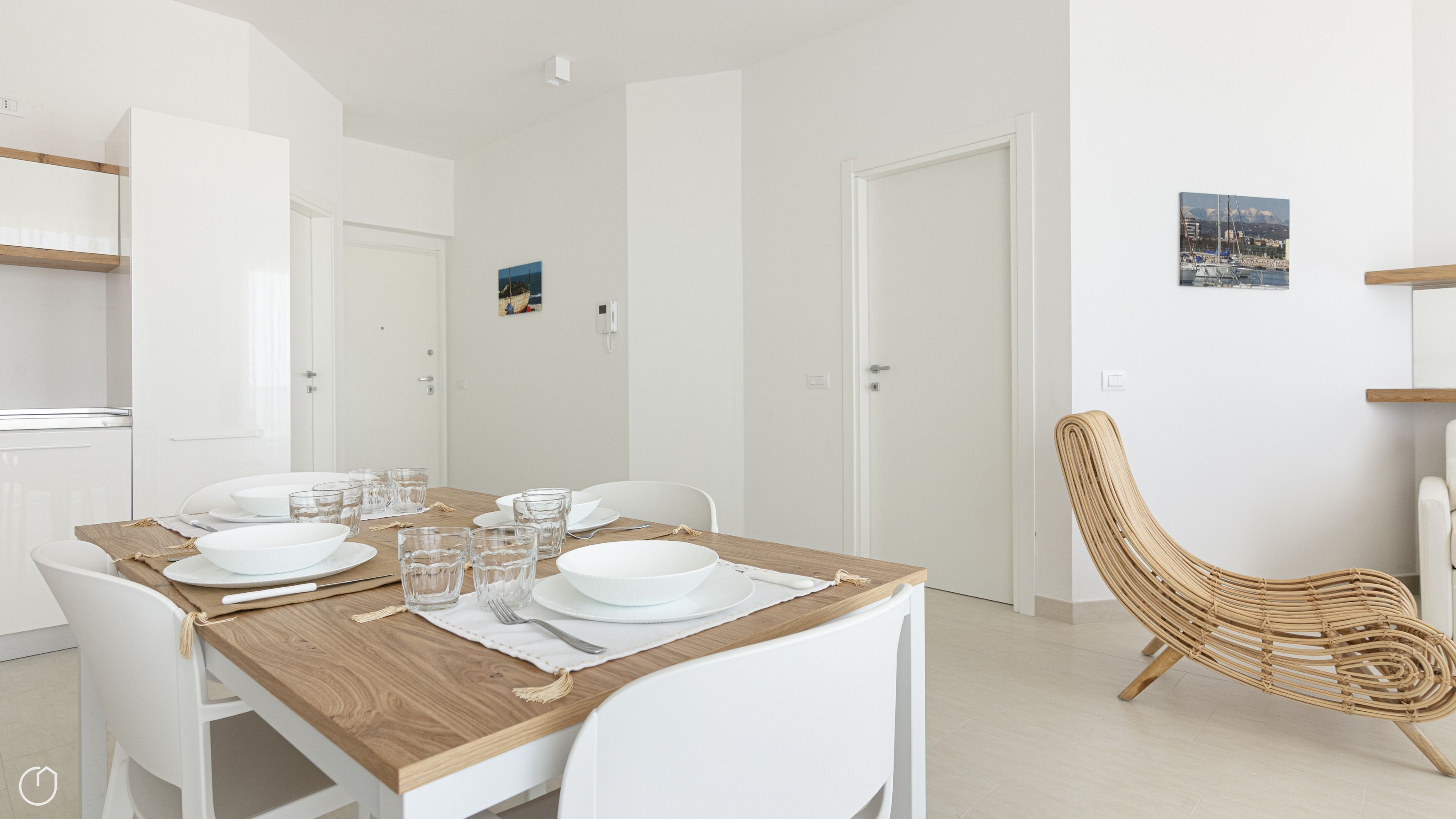 A modern dining area with a wooden table set for four, white chairs, and a wicker chair.