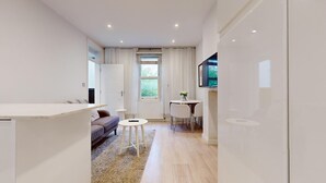 Een moderne, goed verlichte kamer met een bank, een klein rond tafeltje en een aan de muur bevestigde televisie.
