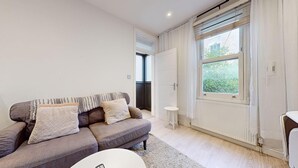 Een moderne woonkamer met een grijze bank, een kleine witte tafel en een groot raam met uitzicht op groen.