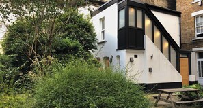 Une maison moderne à deux étages, dotée d’une façade blanche et de moulures noires, et entourée d’une végétation luxuriante.