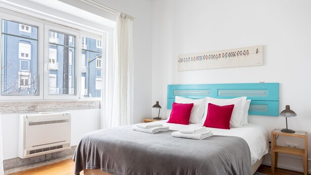 A bedroom with a bed, a window, a wall-mounted air conditioner, and a nightstand with a lamp. - Casa da Avenida I in Lisboa (Lisbon)