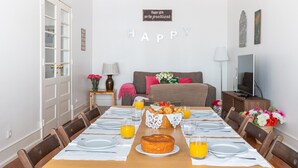 A dining area with a long table set for a meal, a bed with pillows, a TV, and a wall sign. - Casa da Avenida I in Lisboa (Lisbon)