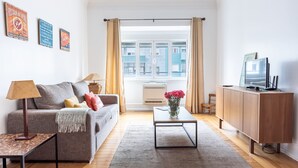 A living room with a sofa, coffee table, TV, and a view of buildings outside. - Casa da Avenida III (Lisbon)