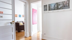 A hallway with wooden flooring, a grey sofa, and a pink wall with a clothing-related poster. - Casa da Avenida III (Lisbon)