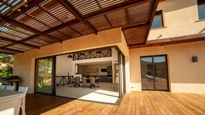 Ein modernes Haus mit einer Holzdiele, einer Glastür, die in einen Essbereich führt, und Blick auf die umliegende Landschaft.
