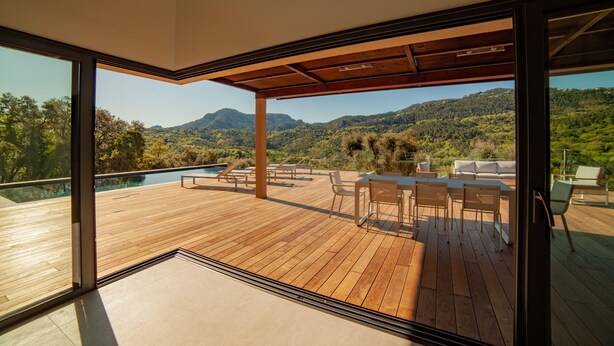 Eine Holzterrasse mit Gartenmöbeln, einem Pool und einer schönen Bergblick.