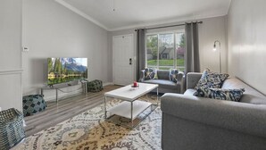 A modern living room with a flat-screen TV, grey sofa, patterned rug, and a ceiling fan. - Easy Livin` By Easton: Hot tub, Family Friendly, 6 minutes from Easton Town Center (Columbus)