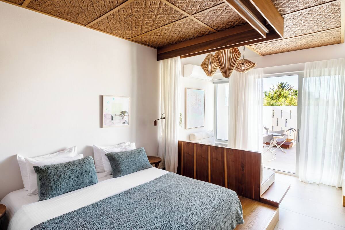 A bedroom with a bed, a wooden headboard, a nightstand, and a window with curtains.