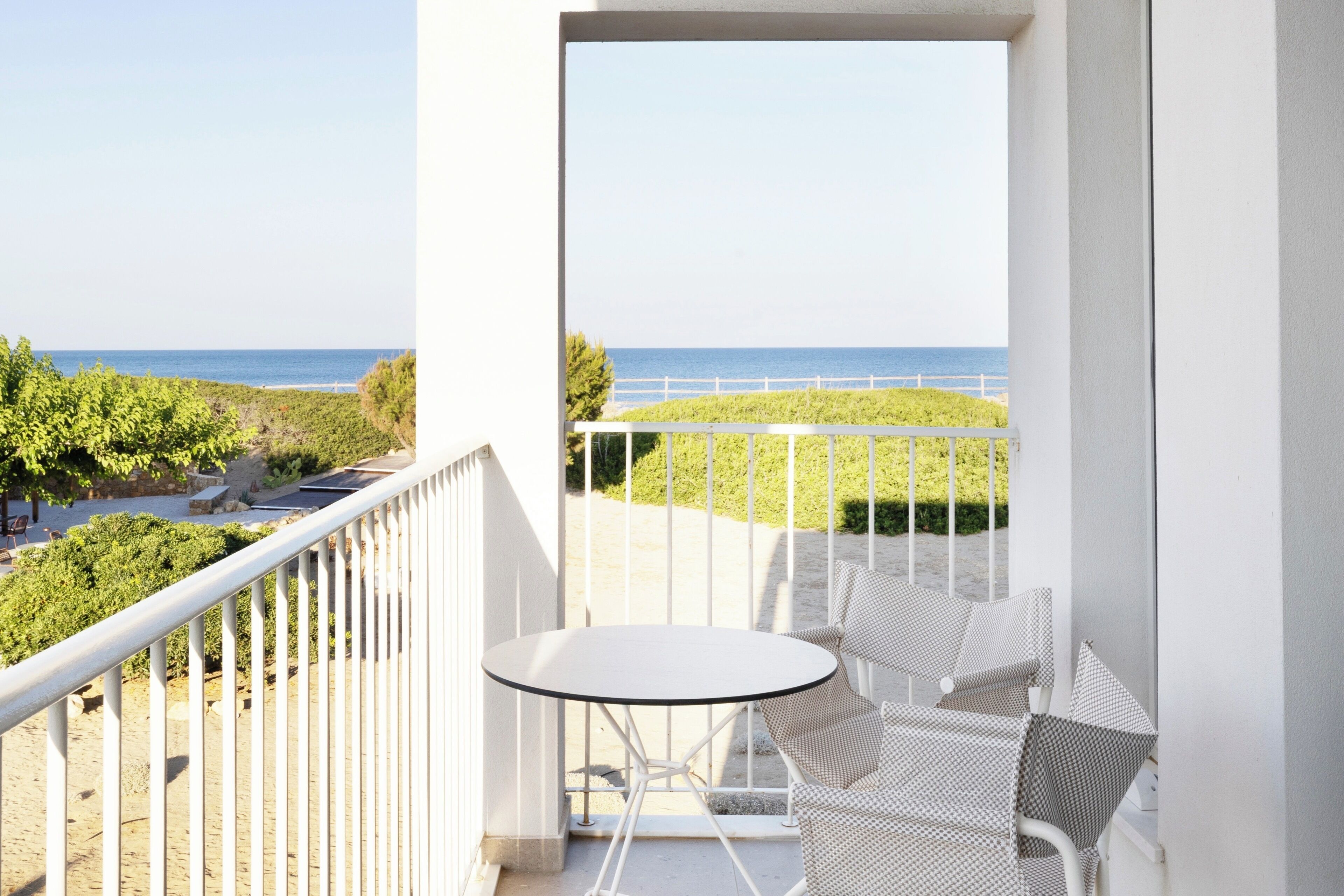 A balcony with a white railing, a small round table, and two wicker chairs.