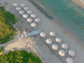 An aerial view of a beach with rows of sun loungers and umbrellas, a wooden walkway, and clear turquoise water. - ALERO Seaside Skyros Resort (Skiros)
