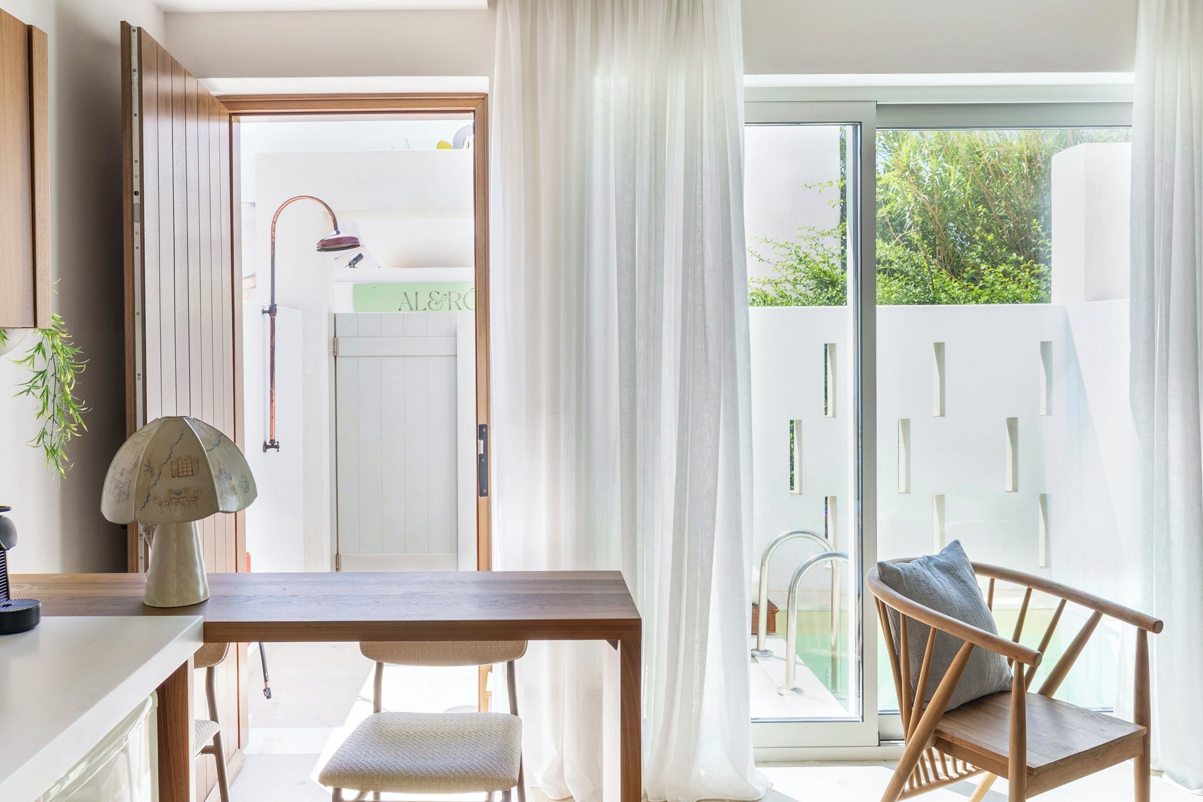 Una cocina moderna con una mesa y sillas de madera, un armario blanco y vistas a un jardín verde a través de una puerta de vidrio.